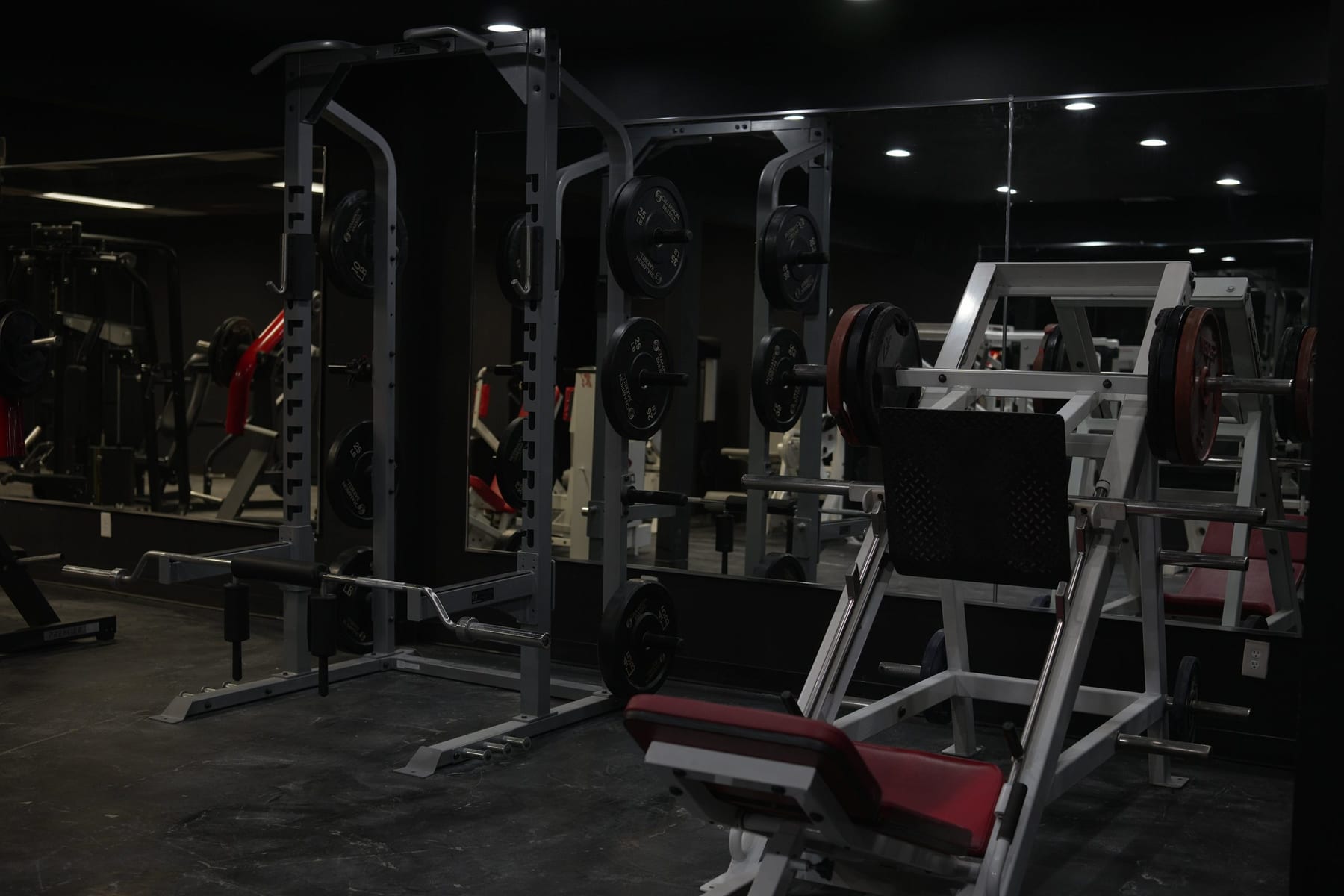 Two power racks with plates next to a red-padded leg press