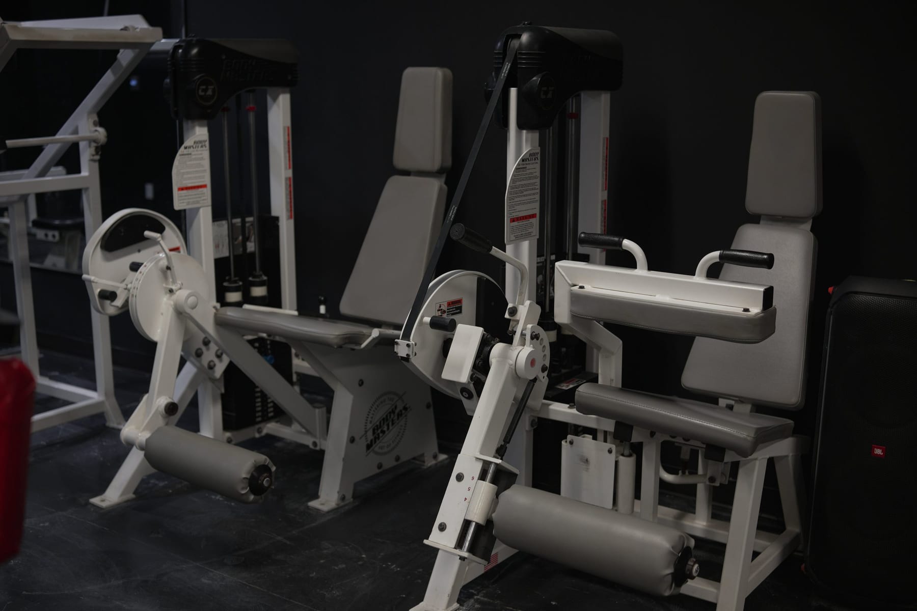 Two classic white leg-extension machines against a black wall